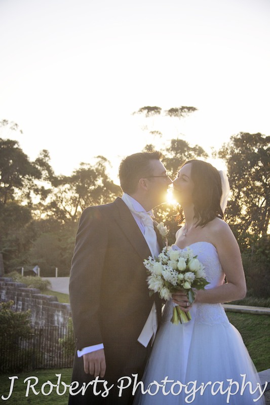 Bridal couple kissing in front of the setting sun - wedding photography sydney